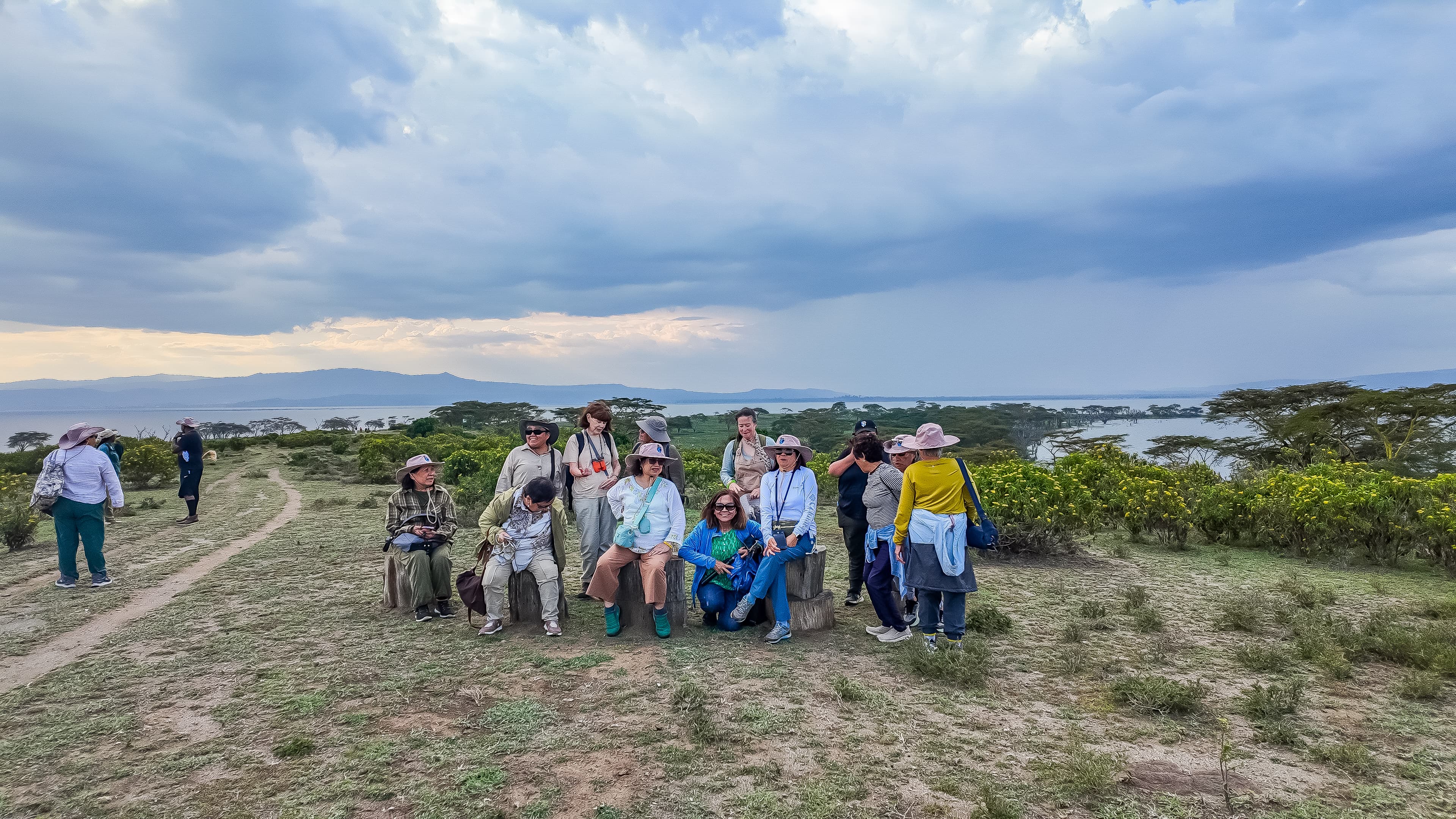 Beyond the Plains Safaris guests at a scenic lakeside viewpoint during an East Africa safari, with acacia trees and mountains in the background