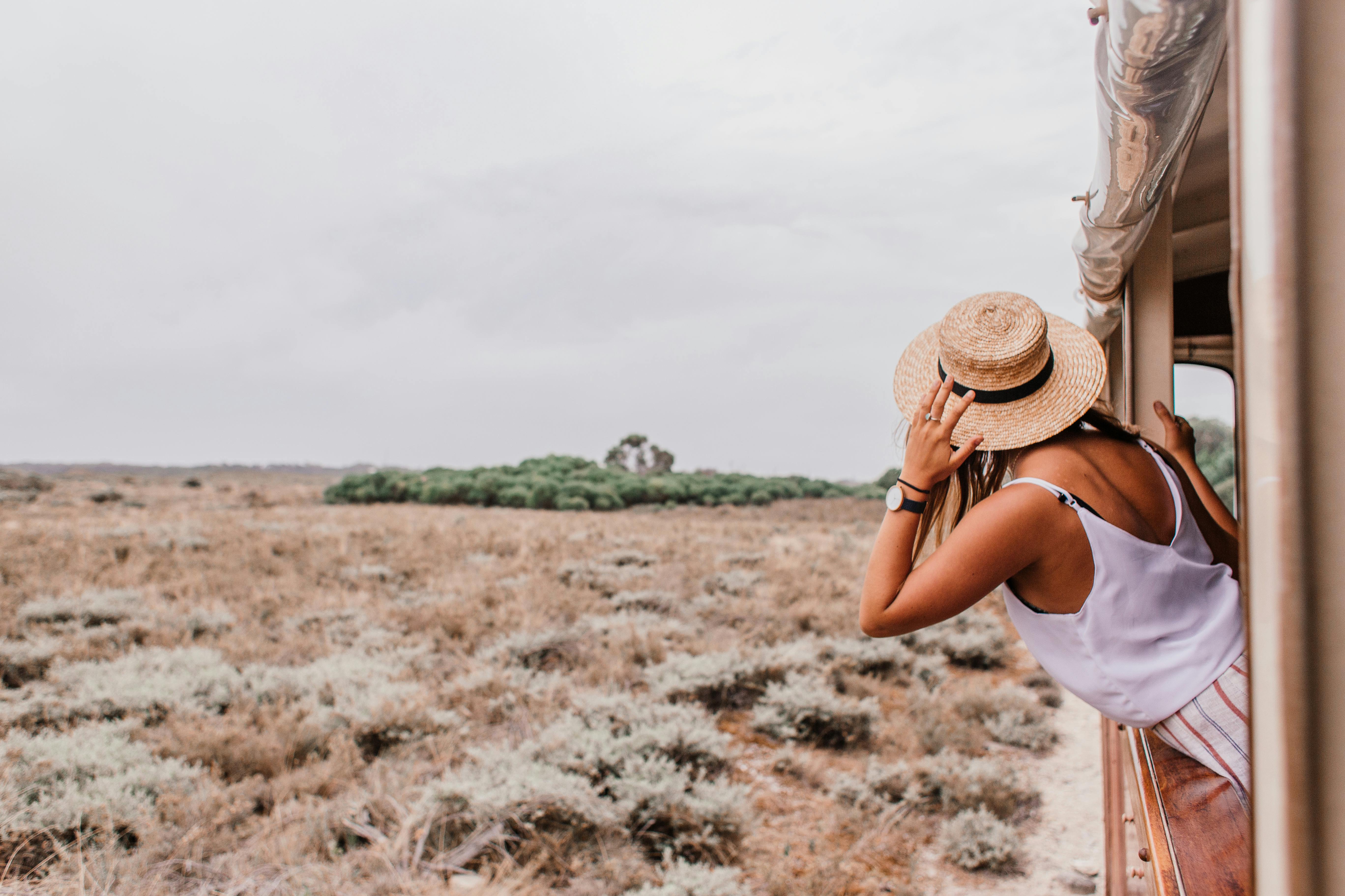 Woman in a straw hat leaning out of a safari vehicle window looking across open dry savanna grassland