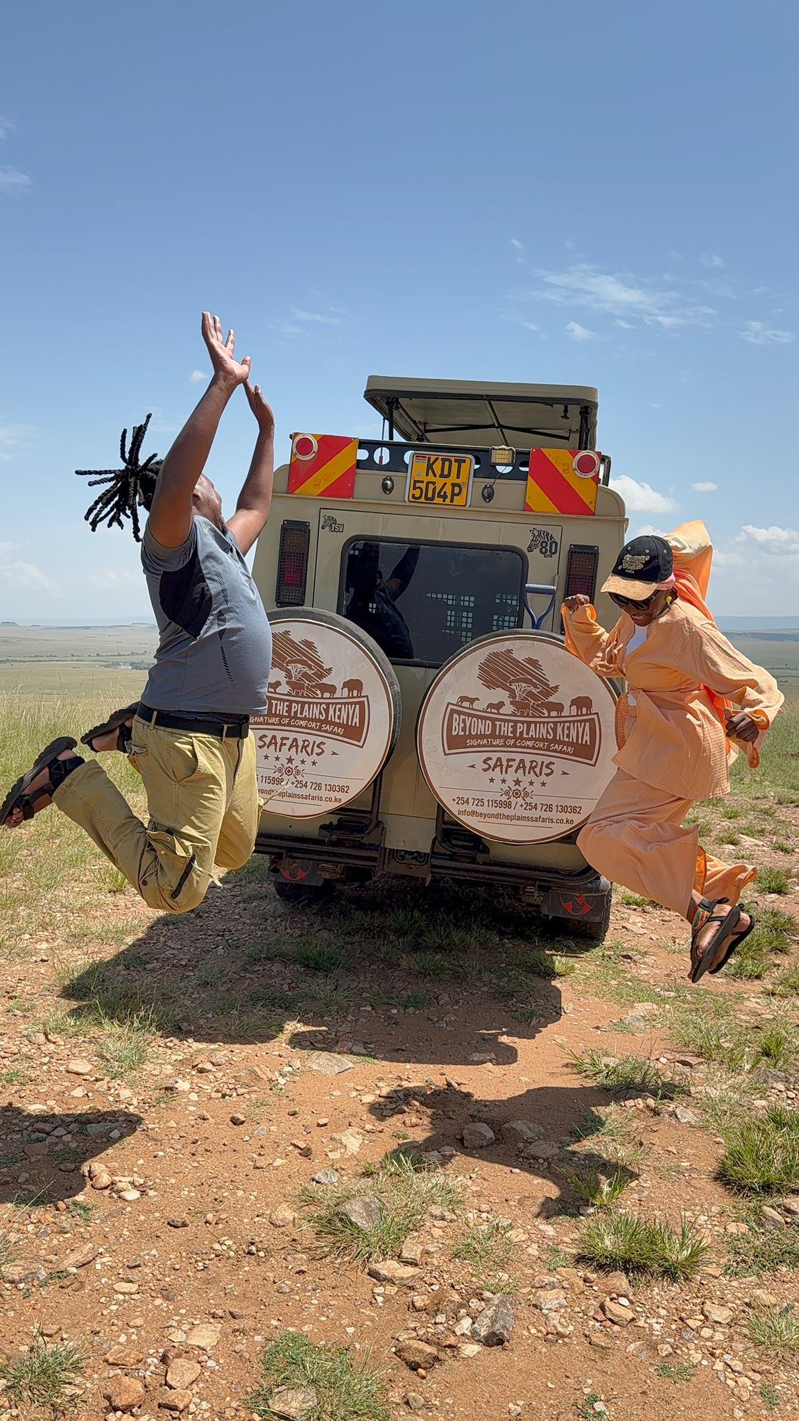 Two happy Beyond The Plains Safaris clients jumping for joy behind a safari vehicle on the Masai Mara plains, Kenya