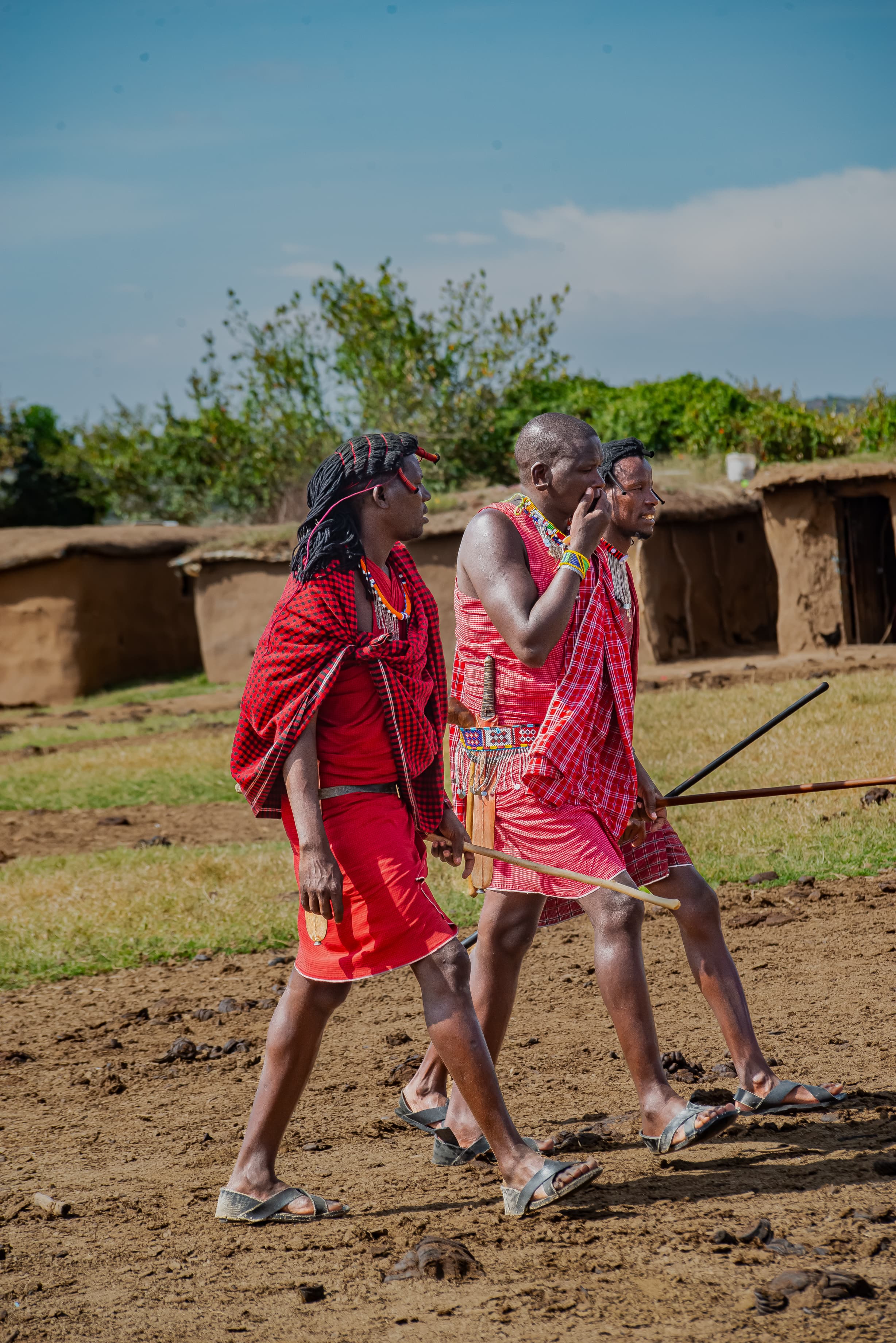 Maasai warriors walking through a manyatta village enclosure with traditional mud homes in the background, Kenya safari cultural visit