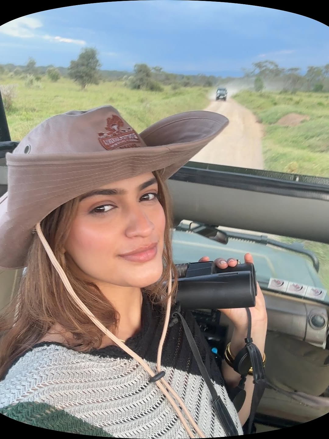 A safari guest holding binoculars on an open-roof game drive vehicle in the East African savannah