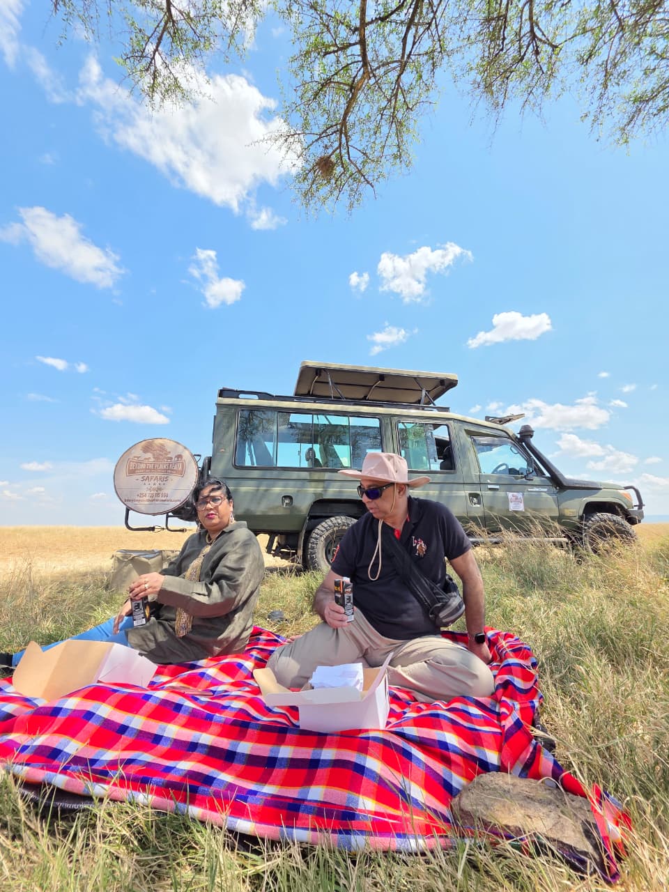 Clients enjoying a bush picnic lunch on the savannah with a Beyond the Plains Kenya safari vehicle in the background