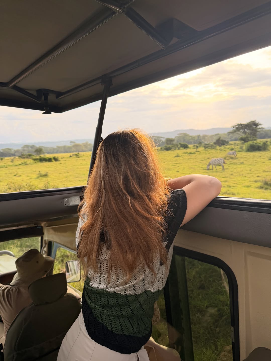 Safari client watching zebra grazing from an open-roof 4WD game drive vehicle on the Kenyan plains