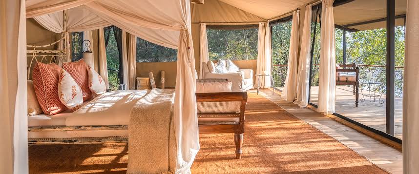 Interior of a luxury safari tent at Serian Mara North with elegant canopy beds and a private bush-view deck.
