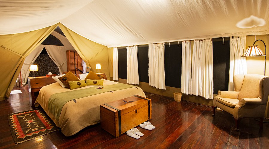 Luxury safari tent interior at Karen Blixen Camp with elegant bedding, wooden floors, and cozy seating.