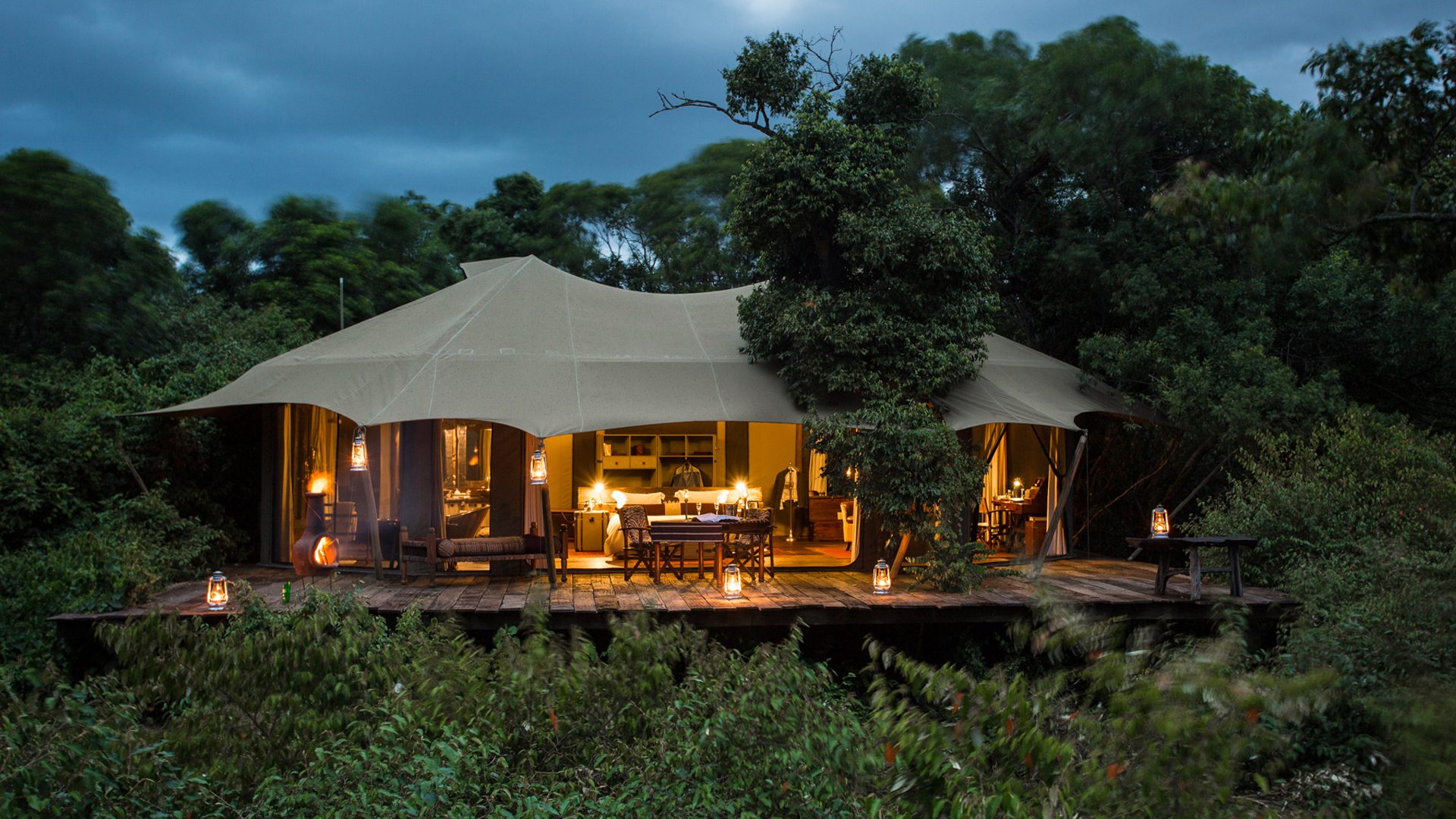 Luxury safari tent at Mara Plains Camp glowing at dusk, surrounded by dense forest in the Maasai Mara.