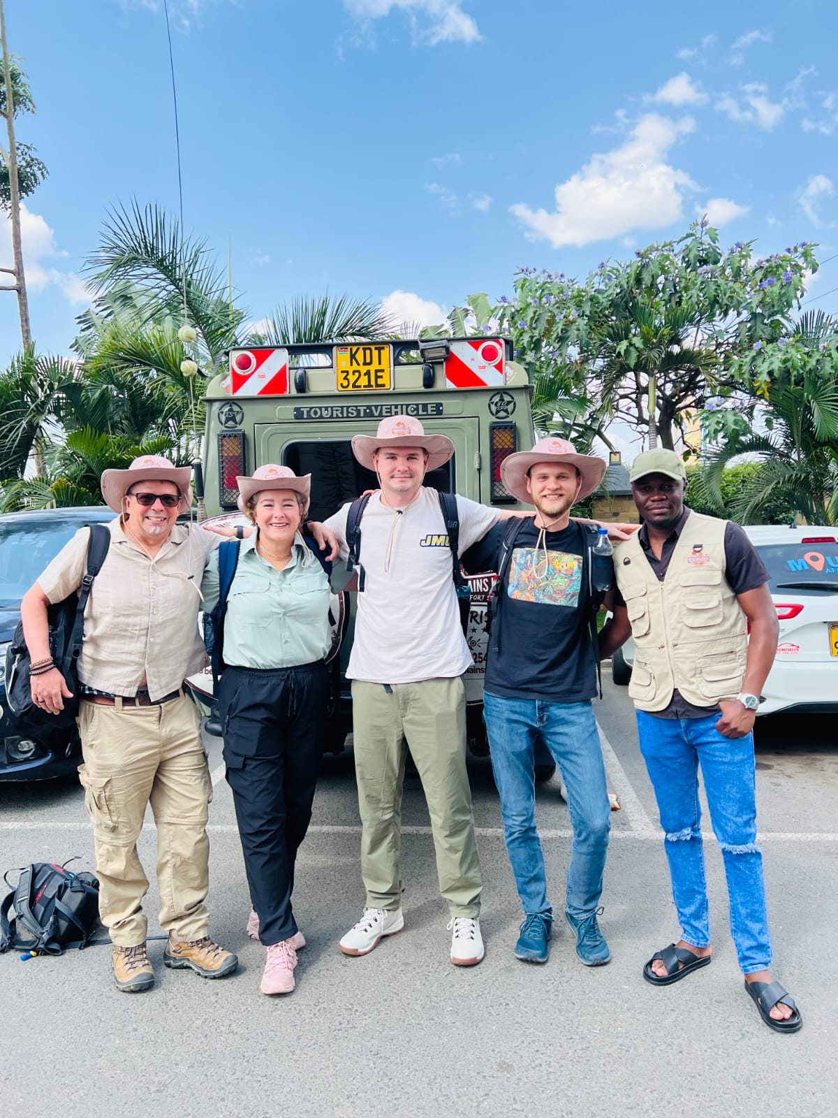 Family reunion safari group posing with guide in front of Kenya safari vehicle
